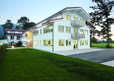 Modernes, weißes Bürogebäude von OilDoc in grüner Landschaft, Außenansicht des Hauptsitzes in Brannenburg in der Abenddämmerung