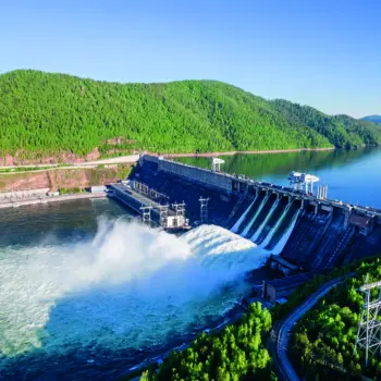 Großes Wasserkraftwerk mit Staudamm, ablaufendem Wasser und umgebenden Wäldern bei klarem Himmel, Luftaufnahme