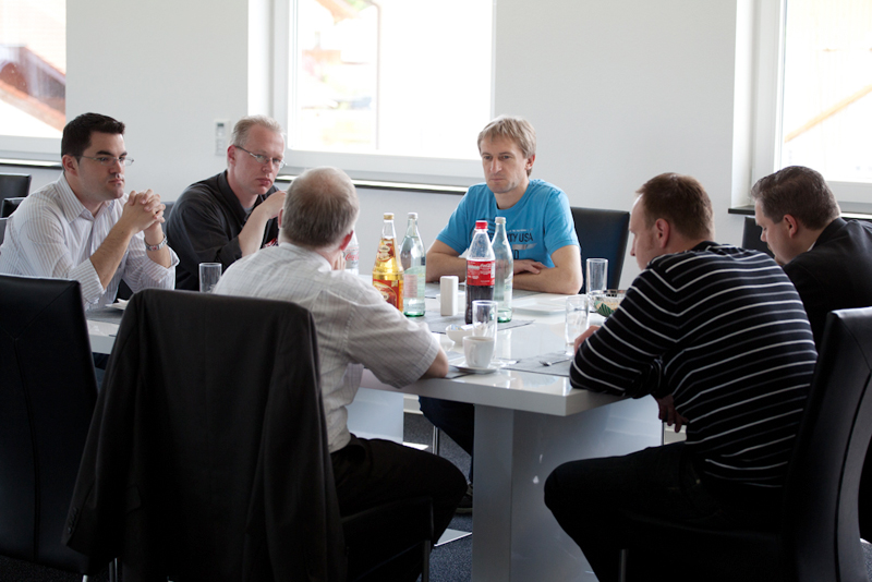 Gruppe von Seminarteilnehmern sitzt an einem Tisch im Pausenraum, spricht miteinander und hat Getränke und Tassen vor sich stehen.