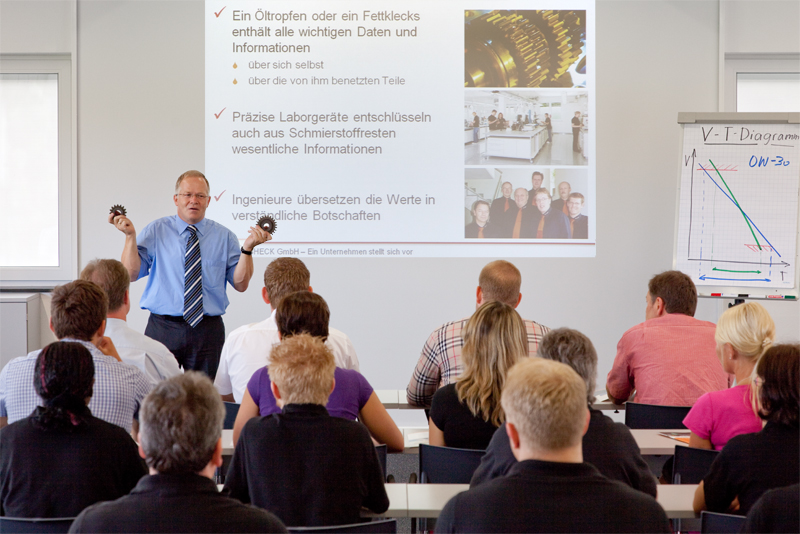 Referent steht vor einer Präsentationsfolie zu Öltropfen, Laboranalyse und Ingenieurleistungen und erklärt einer Gruppe von Teilnehmenden die Inhalte.