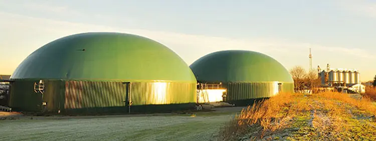Biogasanlage im Morgenlicht – sichere Schmierung für BHKW, Rührwerke und Getriebe Zwei grüne Fermenter-Kuppeln einer Biogasanlage in ländlicher Umgebung bei Sonnenaufgang