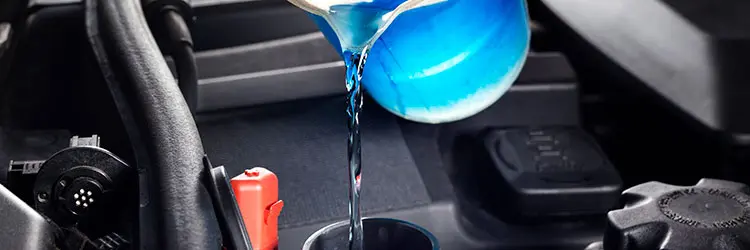 Kühlerfrostschutzmittel – blaues Kühlmittel korrekt in den Motor einfüllen Blaues Kühlerfrostschutzmittel wird aus einem Messbecher in den Kühlkreislauf eines Motors eingefüllt