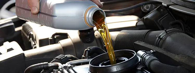 Höherer Ölverbrauch durch neues Motorenöl? Ursachen erkennen und bewerten Goldenes Motoröl wird aus einem Kanister in einen Pkw-Motor eingefüllt, Symbolbild für veränderten Ölverbrauch nach Ölwechsel