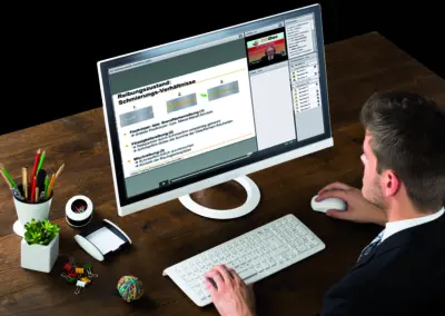 Geschäftsmann sitzt am Schreibtisch und nimmt an einem OilDoc Online-Training zur Schmierung und Reibungszuständen an einem großen Monitor teil