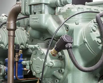 Mehrere grüne Industriekompressoren mit Rohrleitungen und Anbauten in einer Anlagehalle