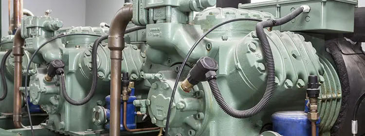 Kompressoren richtig schmieren – Kompressorenöl für zuverlässige Industrieanlagen Mehrere grüne Industriekompressoren mit Rohrleitungen und Anbauten in einer Anlagehalle