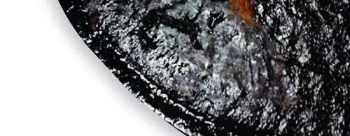 Dunkle, festhaftende Ablagerungen und Beläge als Beispiel für Varnish und Ölschlamm auf einer Metalloberfläche